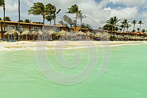 Beautiful view of white sand Aruba beach. Blue sunbeds under sun umbrellas on turquoise water and blue sky.