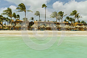 Beautiful view of white sand Aruba beach. Blue sunbeds under sun umbrellas on turquoise water and blue sky.