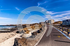 Beautiful view Woljeong Beach besides trunk road providing leading line at Jeju Island South Korea with white windmill at far left