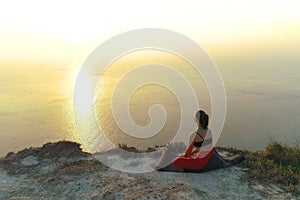 Beautiful view of woman doing yoga meditation on the mountain with sea view at sunset.