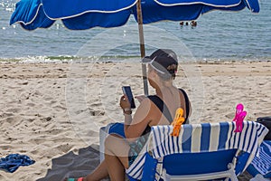 Beautiful view of woman sitting on sun lounger on sandy beach and surfing on her mobile phone.