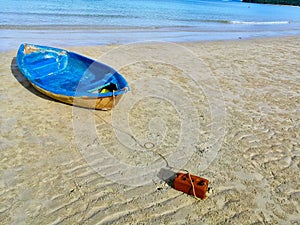 Beautiful view with wooden blue fishing boat tied with rope to brick on sand beach with blue sea background