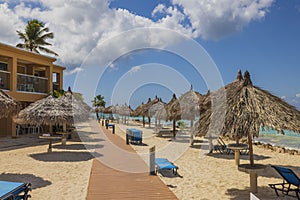 Beautiful view of wooden path between hotel buildings and sun umbrellas on beach along coastline.