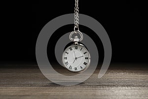 Beautiful vintage pocket watch with silver chain on black background above wooden table. Hypnosis session