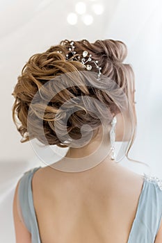 Beautiful volume hairstyle for a bride in a gentle blue light dress with large earrings and adornment in hair