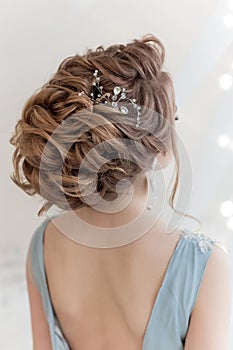 Beautiful volume hairstyle for a bride in a gentle blue light dress with large earrings and adornment in hair