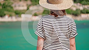 Beautiful warm summer scene - woman in striped t-shirt and hat standing on turquoise sea background. Girl on pier in