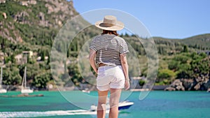 Beautiful warm summer scene - woman in striped t-shirt and hat standing on turquoise sea background. Girl on pier in