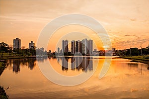 A beautiful warm sunset at the lake with buildings and the city background. Scene reflected on water.