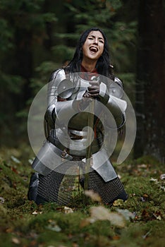 A beautiful warrior girl with a sword wearing chainmail and armor in a mysterious forest.