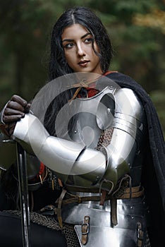 A beautiful warrior girl with a sword wearing chainmail and armor in a mysterious forest.