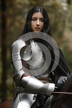 A beautiful warrior girl with a sword wearing chainmail and armor riding a horse in a mysterious forest.