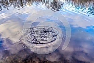 Beautiful water at a lake with splashing water and ripples on the surface with clouds and blue sky reflections