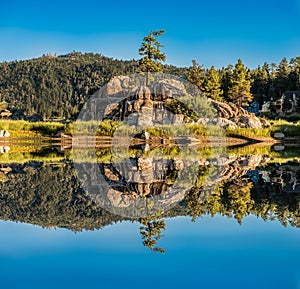 Beautiful water reflection of huge rocks and green trees with a clear blue sky