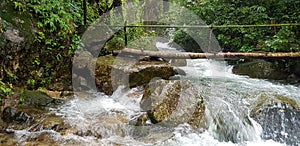 Beautiful waterfall flowing with big rock, green tree, big rock and wooden bridge for across in deep tropical jungle or forest