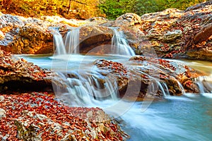 Beautiful waterfall in forest at sunset. Autumn landscape, fallen leaves