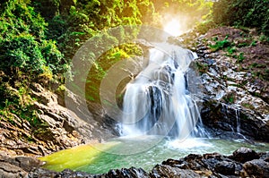 Beautiful waterfall at the mountain with blue sky and white cumulus clouds. Waterfall in tropical green tree forest. Waterfall