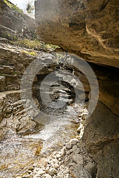 A beautiful waterfall in a mountain gorge with rocks and clear water on a sunny summer day.