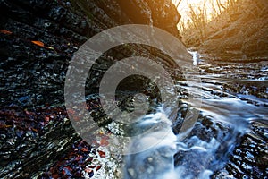 Beautiful waterfall at mountain river in colorful autumn forest with red and orange leaves at sunset. Nature landscape