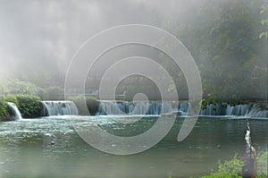 Beautiful waterfall on small cliff with thick fog in the park