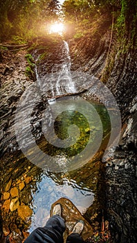 Beautiful waterfall with sunlight in autumn forest. Waterfall vertical panorama. Traveler man stands in front of waterfall river