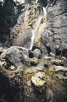 Beautiful waterfall with trees, red leaves, rocks and stones in autumn forest