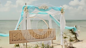 Beautiful wedding arch on the beach. Wooden nameplate with the names of the bride and groom. Wedding day.