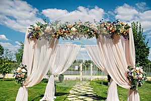 Beautiful wedding arch, decorated with biege cloth and flowers