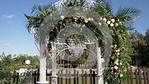Beautiful wedding arch decorated with flowers and palm leaves develops in the wind