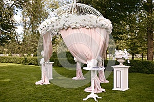 Beautiful wedding arch in the form of a tent on a green lawn, decorated with white flowers