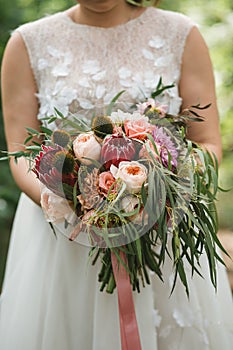 A beautiful wedding bouquet with eucalyptus, roses and exotic flowers in the hands of the bride in a wedding dress.