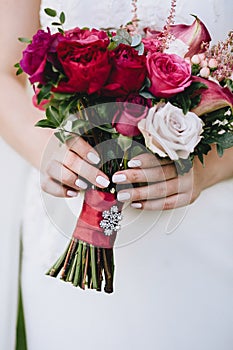 Beautiful wedding bouquet of fuchsia of roses in the hands of the bride with a beautiful manicure. Vertical