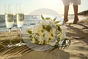 Beautiful wedding bouquet, glasses of champagne and bride on sandy beach