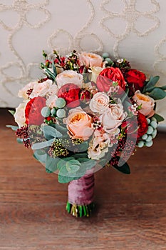 Beautiful wedding bouquet of red flowers, pink flowers and greenery is on the wooden floor.