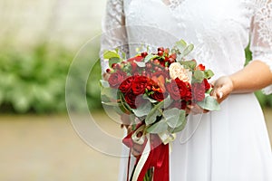 Beautiful wedding bouquet of red roses and red Hypericum berries in hands of bride