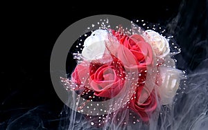 Beautiful wedding bouquet of red and white roses in the fog. White watercolor ink in water on a black background