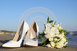 Beautiful wedding bouquet and shoes on sandy beach
