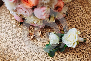 Beautiful wedding bouquet, two gold rings, boutonniere, lying on the armchair, wedding day. Important holiday accessories