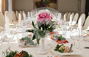 Beautiful wedding bouquet of white and pink peonies in white vase on dinner table in blur. Table setting at luxury wedding