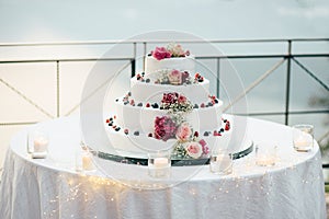 A beautiful wedding cake in four levels is on the table against the background of the picturesque lake