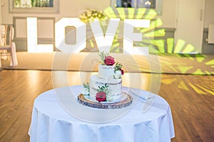 Beautiful wedding cake with rose decorations on a table near a large LOVE sign