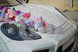 Decorated with flowers as for a wedding . Fresh flowers on the car. Beautiful wedding bouquet on white wedding car . Beautiful