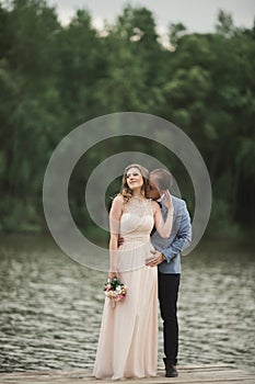 Beautiful wedding couple, bride,groom kissing and posing on the bridge near lake