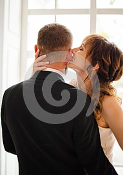 Beautiful wedding couple in bright room. They kiss and hug each other