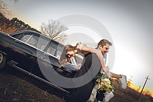 Beautiful wedding couple in the countryside next to the retro car. man groom is taking holding bride in his arms. smiling happy ch