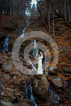 Beautiful wedding couple hugs on the waterfall, Autumn forest background