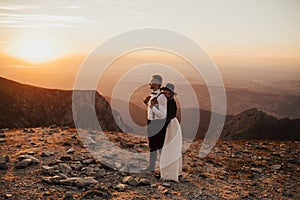 Beautiful wedding couple standing on the top of the mountain in sunset light