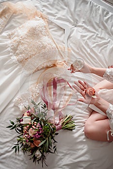 A beautiful wedding dress lies on the bed next to the bride`s bouquet
