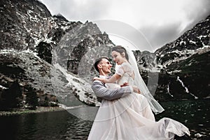 Beautiful wedding photosession. The groom circles his young bride, on the shore of the lake Morskie Oko. Poland