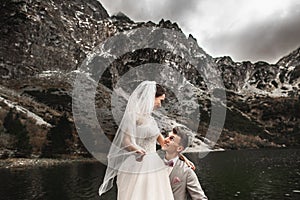 Beautiful wedding photosession. The groom circles his young bride, on the shore of the lake Morskie Oko. Poland